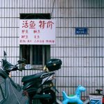 Urban facade featuring a scooter, toy dinosaur, and Chinese sign in a parking area.